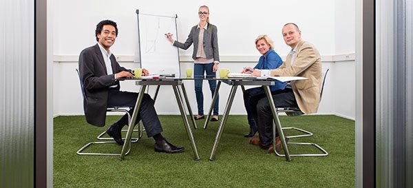 Small business meeting, with four people in a small stylish conference room with grass on the floor, discussing strategy, growth, sustainability and environmental inpact of business,